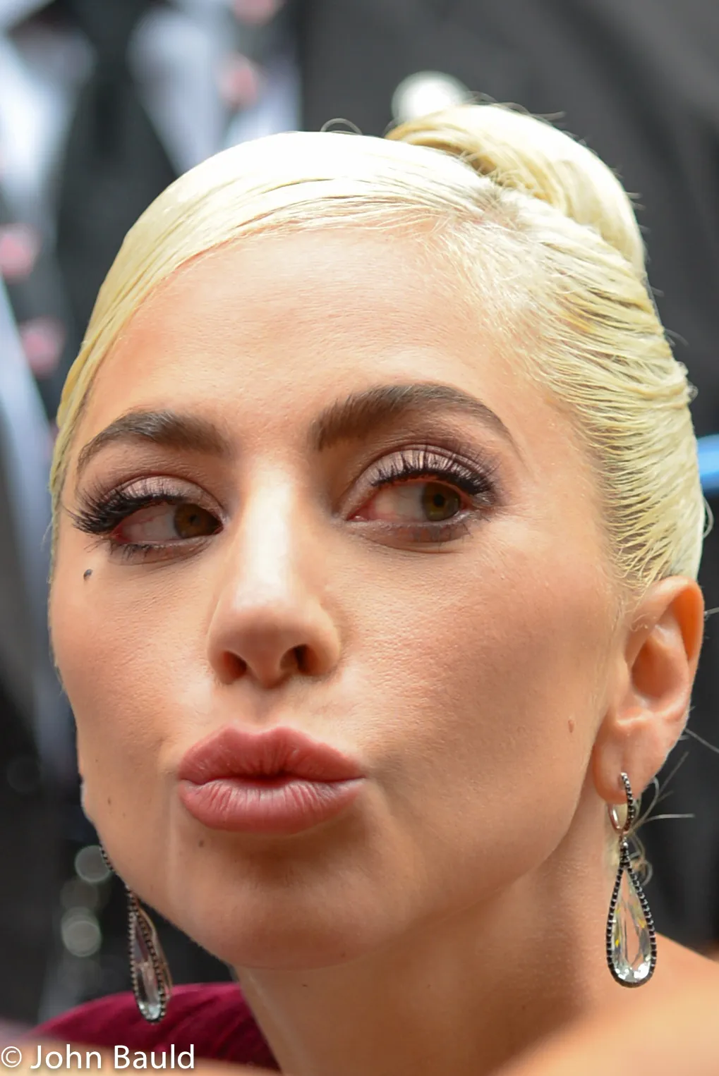 Lady Gaga photographed in 2018 with platinum-blonde hair gathered into a high crown updo.